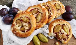 Pyszne drożdżówki ze śliwką, posypane kruszonką, prezentują się apetycznie obok świeżych śliwek.