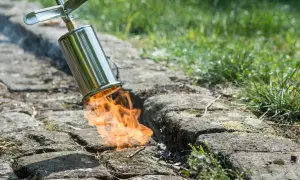 Flammen züngeln aus einem Brenner, um lästiges Unkraut auf einem gepflasterten Weg abzuflammen.