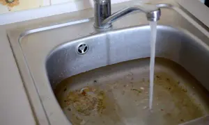 Verstopfter Abfluss im Haus? Salz als Hausmittel könnte helfen. Das Spülbecken ist voller Essensreste und steht unter Wasser.