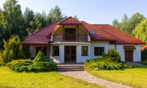 Urokliwa agroturystyka w dolinie stawów. Biały dom z czerwoną dachówką, otoczony zielenią, zaprasza na wypoczynek.