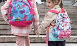 Dwie dziewczynki w kolorowych plecakach szkolnych trzymają się za ręce na schodach.
