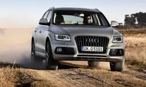 Srebrny Audi Q5 z kierowcą w okularach jedzie po piaszczystej drodze, wzbijając kurz. Wiele osób szuka audi q5 opinie przed zakupem.