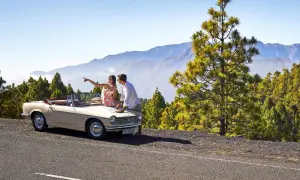 Pareja planeando sus rutas en coche por La Palma, con un descapotable y un paisaje montañoso de pinos.
