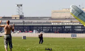 Ein Mann mit nacktem Oberkörper steht auf dem Feld vor dem BERLIN-TEMPELHOF. Ein Gleitschirm liegt im Vordergrund.