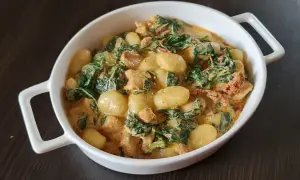 Pyszne gnocchi z kurczakiem w sosie śmietanowym, ze szpinakiem i suszonymi pomidorami, podane w białej misie.