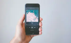 A hand holds a smartphone displaying the Spotify app, showing the song "Peace" by ramp. This image illustrates how to get music on Spotify.