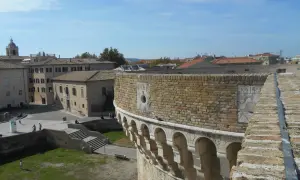 Vista panoramica di Senigallia, Ancona, con un'antica fortezza in primo piano e tetti di tegole rosse sullo sfondo sotto un cielo azzurro.