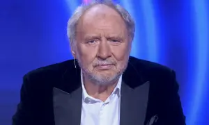 Andrzej Grabowski, znany z wielu niezapomnianych ról w polskich filmach, w eleganckim czarnym garniturze na tle niebieskiego światła.