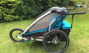 En Thule Chariot Sport 2 barnvagn står på en gräsmatta. Den är blå och svart med stora hjul.