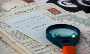 Loupe pour retrouver un acte de décès. Documents anciens, carte et loupe suggèrent une recherche généalogique.
