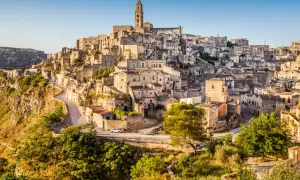 Matera: zobacz starożytne kamienne domy i kościół na wzgórzu. Wąskie uliczki i zielone zbocza tworzą malowniczy krajobraz.