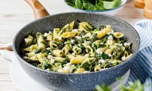 Penne-Nudeln mit Spinat und zerbröseltem Feta in einer Pfanne.