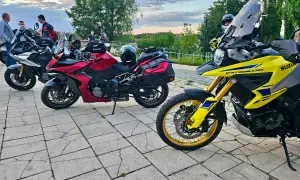 Kilka motocykli Suzuki zaparkowanych na brukowanym placu, z ludźmi w tle.