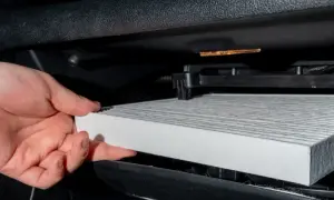 Handen håller ett nytt kupéfilter redo att byta ut det gamla för renare luft i bilen.