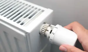 Dłoń kręci termostatem grzejnika, ustawiając temperaturę. Czas zacząć sezon grzewczy.