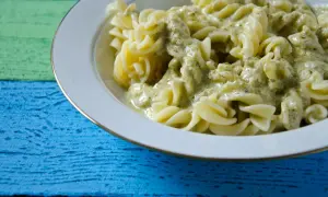 Fusilli-Nudeln in cremiger Pesto Sahne Sauce, serviert auf einem bunten Holztisch.