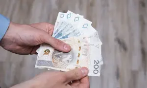 Dłonie trzymają polskie banknoty, w tym 200 zł. Może to symbolizować otrzymanie renty socjalnej z MOPS.
