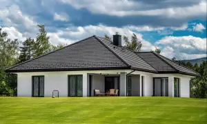 Nowoczesny dom z białymi ścianami i przestronnym, szarym dachem. Na trawniku stoi mała bramka do piłki nożnej.