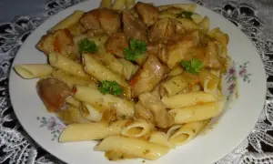 Penne z soczystym makaronem z mięsem wieprzowym w sosie, udekorowane natką pietruszki.
