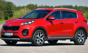 Czerwony Kia Sportage 1. generacji z kierowcą w okularach przeciwsłonecznych jedzie po drodze.