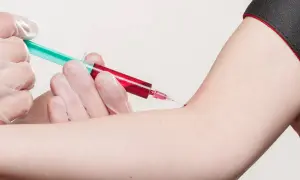 Prélèvement sanguin : une seringue verte et rouge est insérée dans un bras.