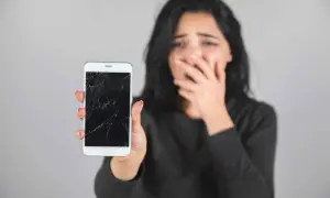 Zrozpaczona kobieta pokazuje pęknięty, czarny ekran w telefonie.