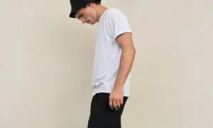 Młody mężczyzna w czarnym kapeluszu typu bucket hat i białej koszulce, spodnie w stylu skate.