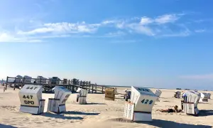 Strandkörbe am St. Peter-Ording Strand unter blauem Himmel. Eine Person entspannt sich im Sand.