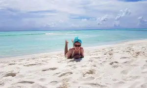 Wrzesień na Malediwach to idealna pogoda na plażowanie. Kobieta w turkusowym turbanie leży na białym piasku, ciesząc się słońcem i błękitem oceanu.