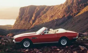 Röd Aston Martin V8 Vantage cabriolet parkerad i en stenig, bergig terräng med en sjö i bakgrunden.