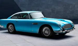 Błękitny Aston Martin DB5 z charakterystycznymi szprychowymi felgami, lśniącym chromem i elegancką linią nadwozia, zaparkowany przed nowoczesną, betonową ścianą.
