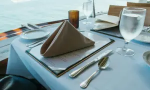 Stół w restauracji z widokiem na morze, nakryty do posiłku, z menu i kieliszkiem wody.