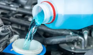 Blaues Scheibenwischwasser wird aus einem Behälter in den Einfüllstutzen gegossen.