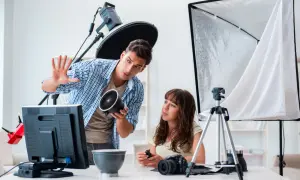 Mężczyzna, technik fotografii i multimediów, pokazuje kobiecie lampę. W tle sprzęt studyjny.