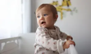 Un bébé aux yeux bleus, prénom fille, se tient dans son lit, curieux du monde.