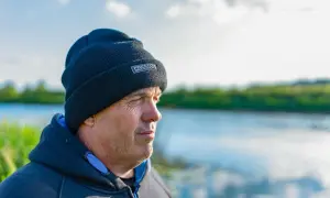 Mężczyzna w czapce Preston Innovations patrzy w dal nad wodą.