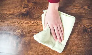 Mano limpiando un suelo de madera con un paño, aprendiendo como quitar manchas de la madera sin dañarla.