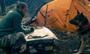 Man och hund vid orange tält, planerar en expedition. Kanske är det hjärtat av besten de söker.