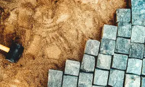 Piasek i brukowa kostka granitowa, obok gumowy młotek.