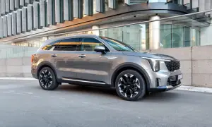 Elegancka, szara nowa Kia Sorento z czarnymi felgami stoi przed nowoczesnym budynkiem.