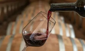 Versando vino rosso in un calice, con botti di legno sullo sfondo. Un calice di vino quanti ml? La risposta è nella degustazione.