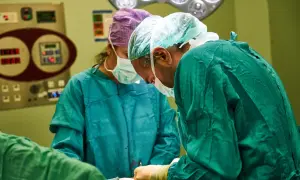 Chirurdzy w zielonych fartuchach wykonują artroskopię barku. W tle widać aparaturę medyczną.