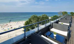 Wygodne fotele i stoliki na tarasie z widokiem na piaszczystą plażę i błękitne morze. Idealne miejsce na relaks, gdy dostępne są wolne pokoje z widokiem na morze.