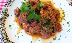 Pyszny bigos z kiszonej kapusty, bogaty w mięso i przyprawy, udekorowany świeżą natką pietruszki.