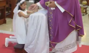 Ksiądz dający komunię dziewczynce w bieli. Wzruszający moment pierwszej komunii świętej.