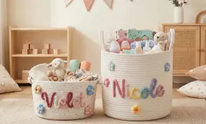 Dwa plecione kosze na zabawki, jeden z napisem "Violet", drugi z imieniem "Nicole", ozdobione kolorowymi kwiatkami i wypełnione pluszakami i akcesoriami dla dzieci.