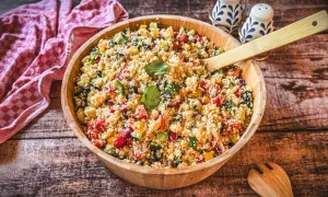 Ein bunter Couscous-Salat mit Feta, Tomaten, Gurken und Paprika, serviert in einer Holzschüssel.