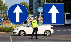 Policjant kieruje ruchem pod znakiem droga jednokierunkowa. Biała strzałka na niebieskim tle informuje o kierunku jazdy.