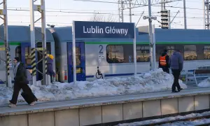 Zimowy dzień na stacji Lublin Główny. Pasażerowie z bagażami czekają na pociąg, a śnieg zalega na peronie.