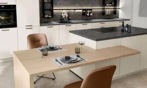 Cocina moderna con encimeras de piedra oscura y gabinetes blancos. La mesa de madera clara y las sillas de cuero marrón complementan los materiales para cocinas modernas.